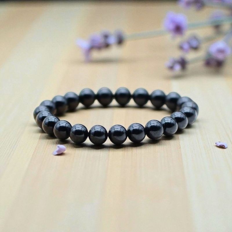 Bracelet en Obsidienne noire présenté sur un fond en bois clair, révélant l'élégance sobre de cette pierre volcanique